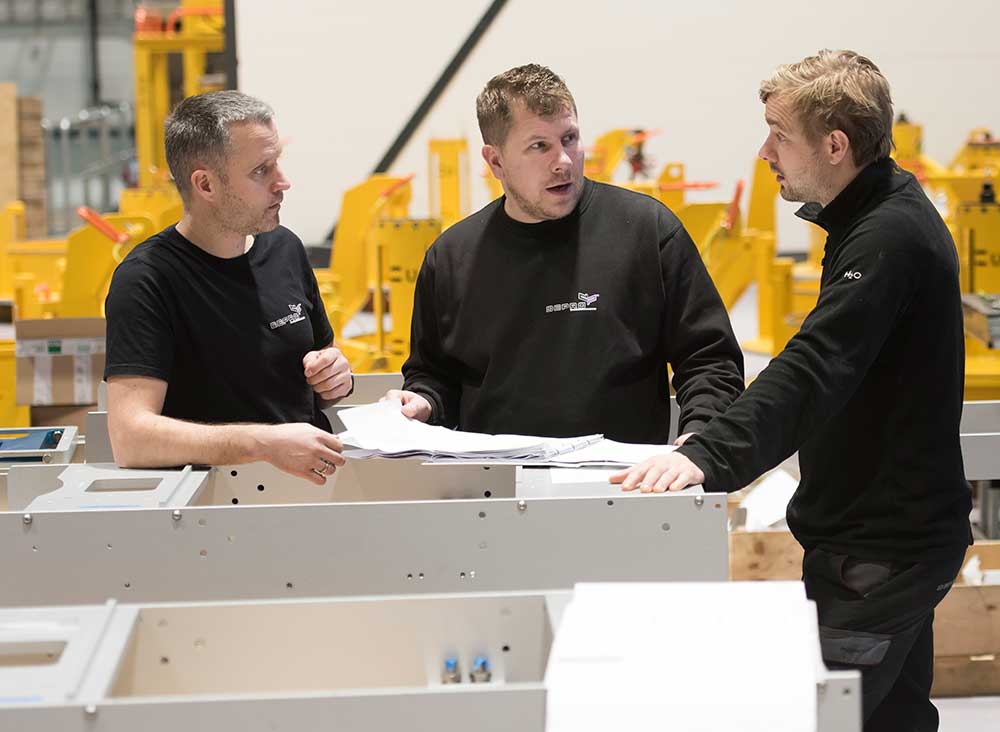 Three men discussing solutions in Depro's workshop.