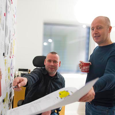 Two male employees look and point at drawings of subsea equipment on a whiteboard.