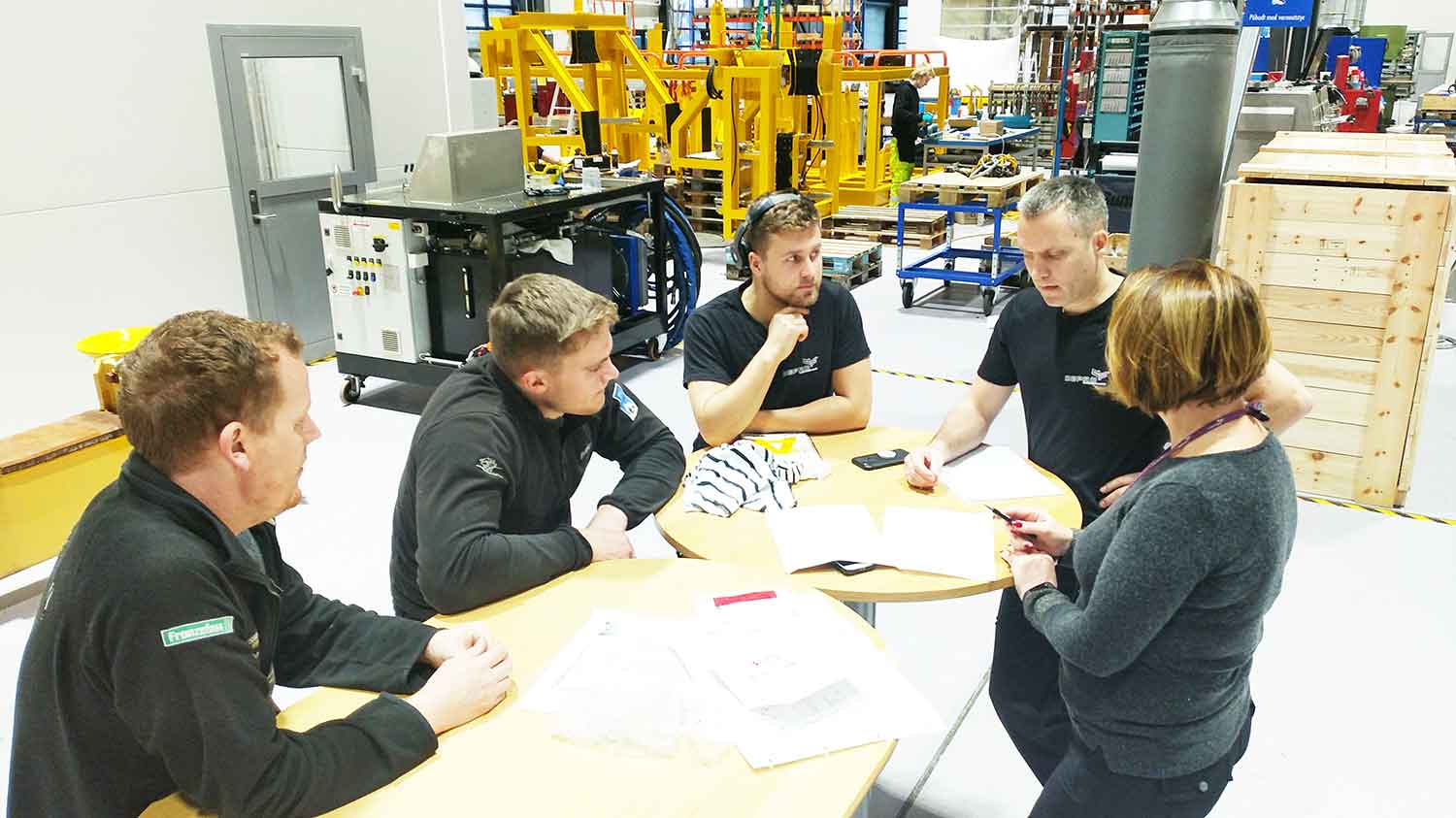 Three men and a woman have a project meeting at a table in Depro's workshop hall.