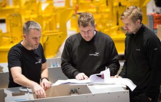 Three men discussing solutions in Depro's workshop.