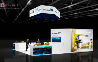 Exhibition booth at OTC in Houston showcasing Depro AS and VideoRay LLC. The booth features a modern, white design with product displays, large branding panels for Depro and VideoRay, a hanging banner above with VideoRay's logo and slogan 'As Tough As Your Mission', and displays of subsea ROV equipment. Two people are interacting at the stand in a spacious, well-lit exhibition hall